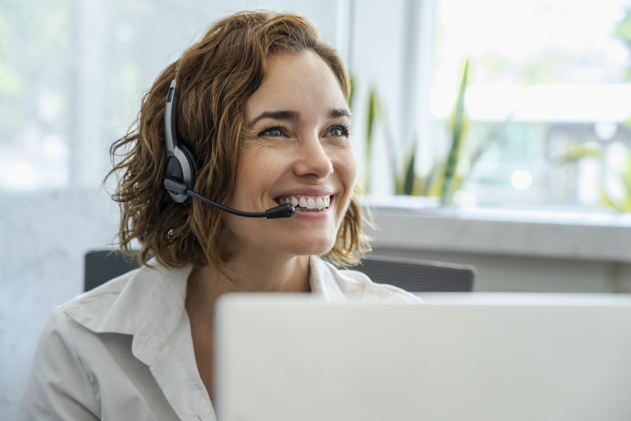 Lächelnde Mitarbeiterin mit Headset am Laptop, Sinnbild für freundliche Erreichbarkeit am Empfang